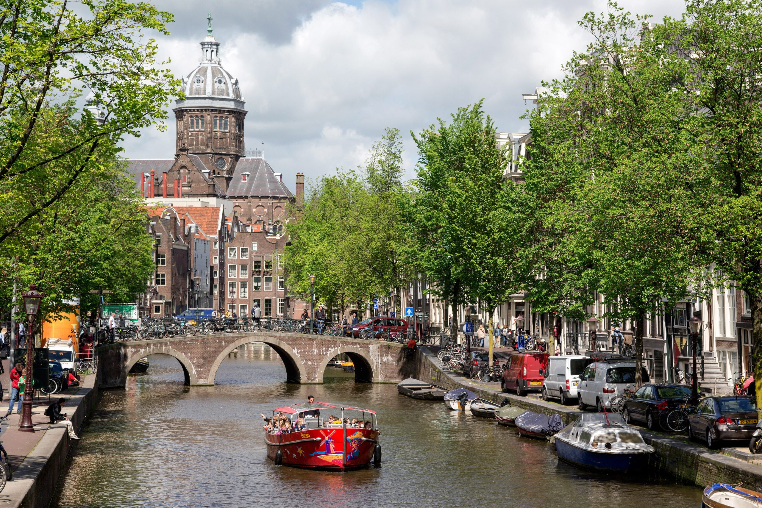 Canal tour boat cruising under a bridge on an Amsterdam canal with historic houses in the background