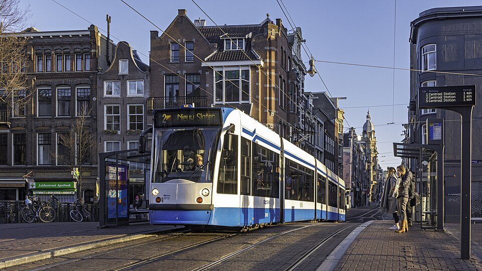 Tranvía azul y blanco de GVB de la línea 2 cruzando el Prinsengracht en Ámsterdam, con casas junto al canal a primera hora de la mañana