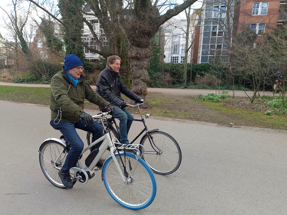 Two people cycling side by side along a path in Vondelpark, Amsterdam