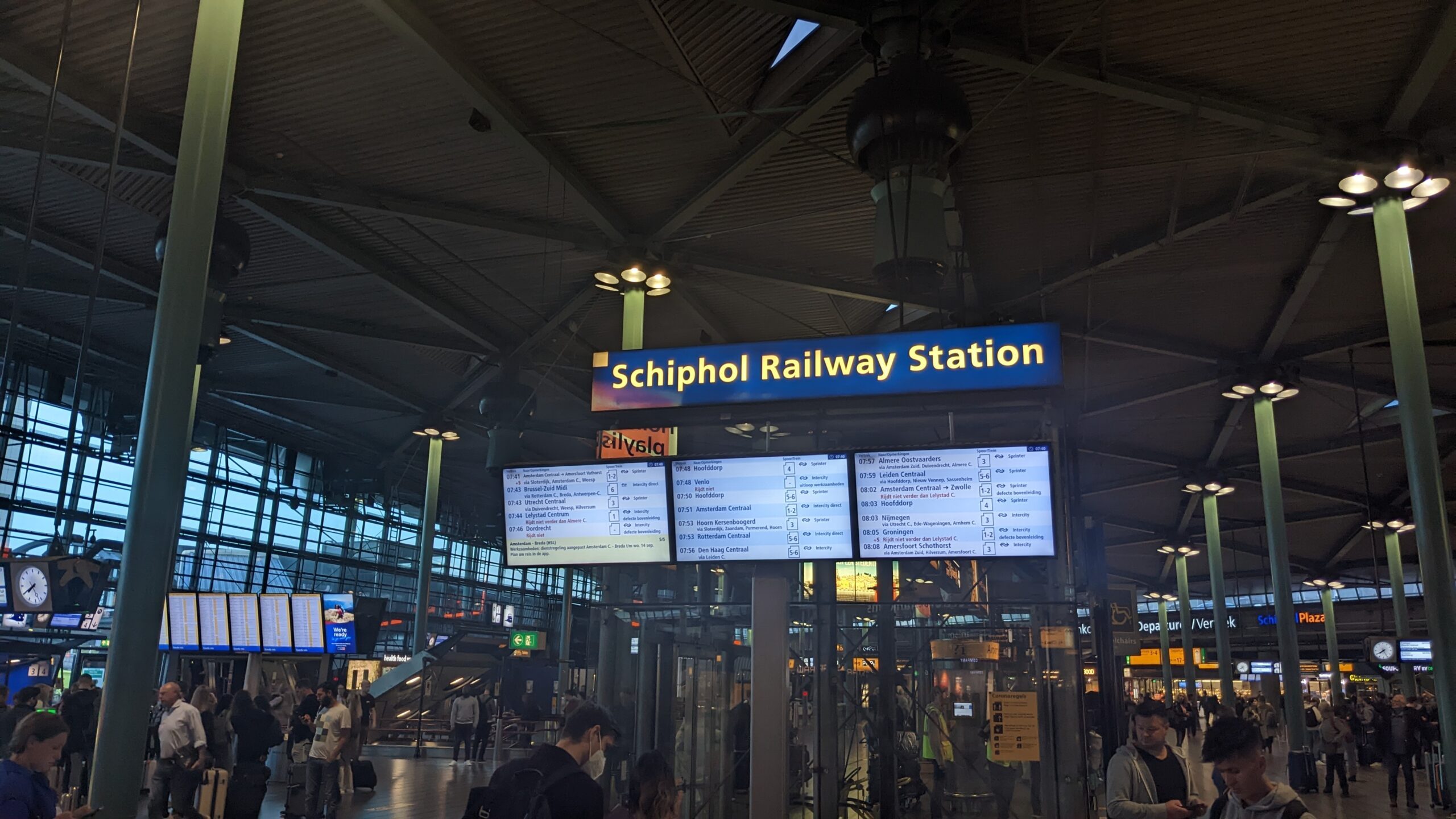Blauw bord Schiphol Railway Station boven de vertrekschermen in Schiphol Plaza op de luchthaven van Amsterdam