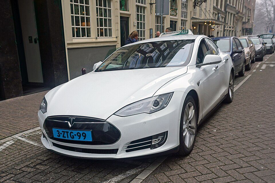 Taxi eléctrico blanco aparcado en una calle adoquinada con casas tradicionales de Ámsterdam