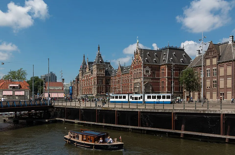 Amsterdam Centraal Station facade under blue sky with a tram passing in front along the water